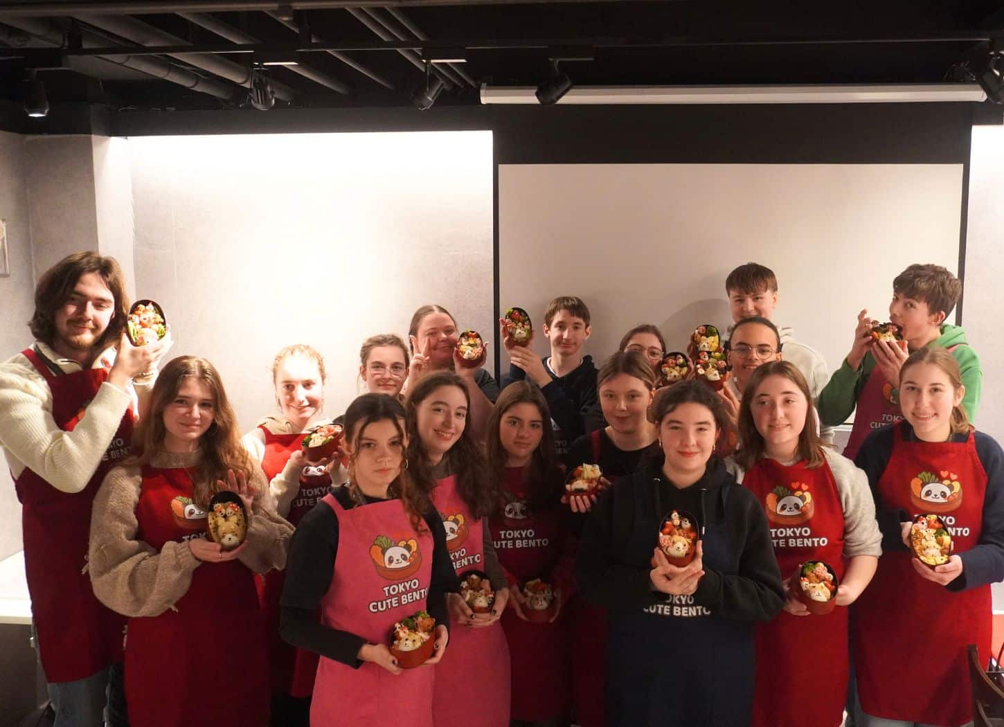 Large group in aprons holding up their finished character bento after a group session