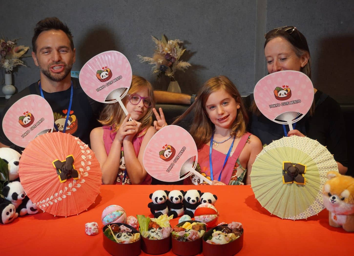 Family posing with Tokyo Cute Bento paper fans and parasols behind their finished character bento